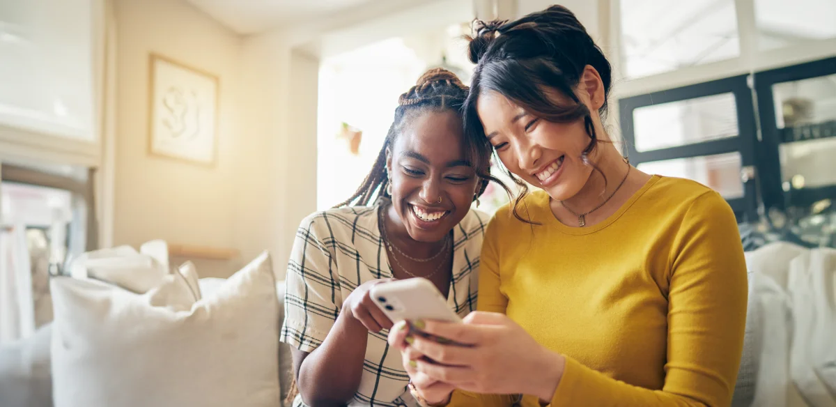 Two students smiling while looking at their phone together